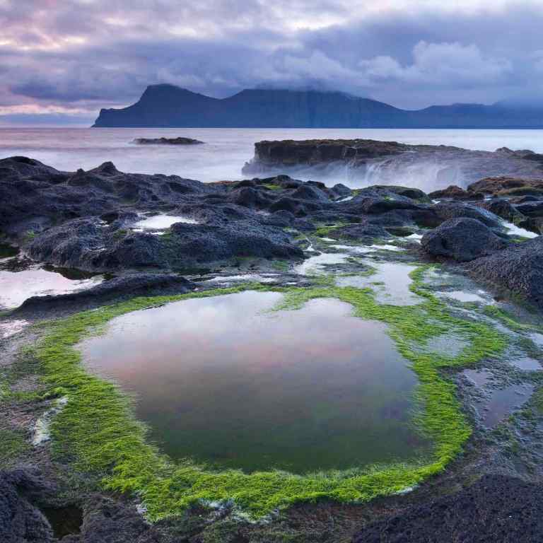 Rockpools on the shores of Gjogv on Eysturoy, looking towards the mountainous island of Kalsoy. Faroe Islands. Spring (June) 2012.